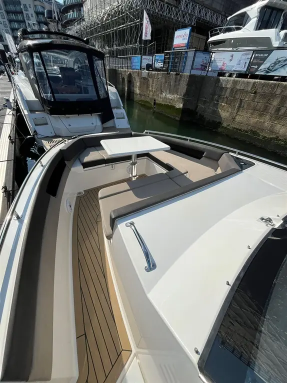 Luxury boat interior featuring a table, upholstered seating, and a modern design, with signs promoting boat services in the background.
